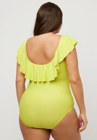 Maillot de bain jaune vif avec un col à volants et un dos ouvert. Tissu lisse et extensible pour une silhouette ajustée.