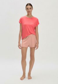 Koralfarbenes Kurzarmoberteil in lockerer Passform, kombiniert mit hellrosa, gerippten Shorts mit einem wellenförmigen Saum. Einfaches, entspanntes Design.