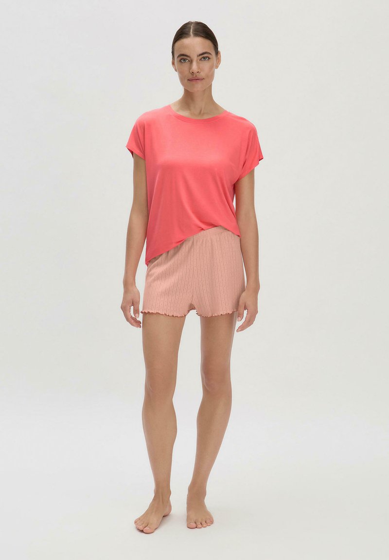 Koralfarbenes Kurzarmoberteil in lockerer Passform, kombiniert mit hellrosa, gerippten Shorts mit einem wellenförmigen Saum. Einfaches, entspanntes Design.