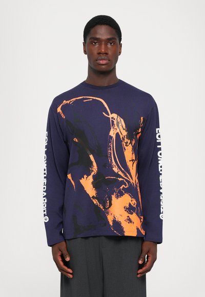 T-shirt à manches longues en bleu marine foncé avec un design graphique abstrait orange. Présente un texte blanc le long de la manche. Fabriqué dans un tissu doux.
