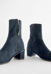 Stivaletti in suede blu navy con tacco quadrato e cerniere laterali. Texture liscia con minima cucitura e design classico.