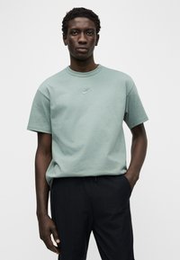 T-shirt de algodão verde claro com gola redonda e mangas curtas, apresentando um pequeno logótipo tonal da Nike no peito. Adequada para uso casual.