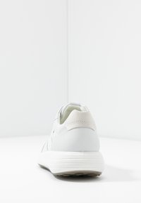 Białe sneakersy z grubą podeszwą pokazane z tyłu, z wyściełanym kołnierzem i przeszyciami w pobliżu pięty.