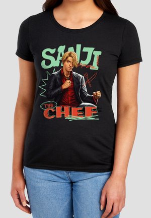 Woman wearing black t-shirt with graphic of blonde man in suit and text "Sanji The Chef" with cooking utensils illustration.