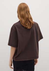Camiseta de algodón marrón de corte holgado, con mangas cortas y escote redondo, de tejido texturizado, llevada sobre una falda de encaje negra.