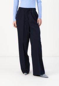 Pantalons larges bleu marine avec une taille élastique à cordon. Fabriqués en tissu lisse, avec un design épuré et sans motifs visibles.