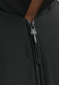 Zwarte jas met een hoge kraag en een halve ritssluiting. Gladde stofstructuur, met een functionele rits met een trekband en stikselaccenten.
