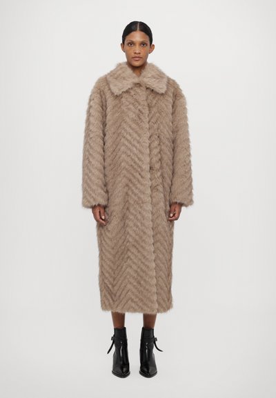 Palton texturat maro în model de herringbone, având un guler larg, mâneci lungi și un design de lungime medie. Poartă peste cizme negre până la gleznă.