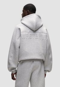 Felpa cropped grigio chiaro con una vestibilità oversize, dotata di cappuccio e testo in rilievo "WRSTBHV" sul retro. Realizzata in tessuto morbido e testurizzato.