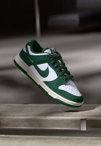 Des baskets Nike Dunk Low en daim vert et cuir blanc, avec une semelle en caoutchouc verte, un bout perforé et des accents de logo dorés.
