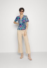 Top de tecido floral em azul marinho e rosa com mangas curtas, combinado com calças largas em tom bege e sandálias de salto bloco em tom rosa.