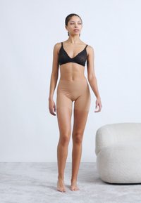 Μαύρο σουτιέν από δαντέλα και μπεζ σορτς με ψηλή μέση, με λεία υφή, ελαστικό υλικό, εφαρμοστή σχεδίαση, μοντέλο στέκεται μπροστά σε ουδέτερο φόντο.