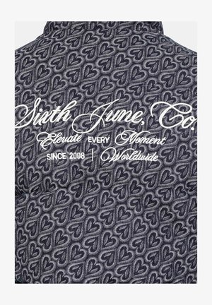 Blaues Stoffmuster mit ineinandergreifenden Herzen; weißer, gestickter Markenname und Slogan im oberen Bereich.