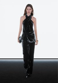 Black velvet halter top with twisted detail, paired with matching black velvet trousers. Model holds a black clutch, smooth texture throughout.