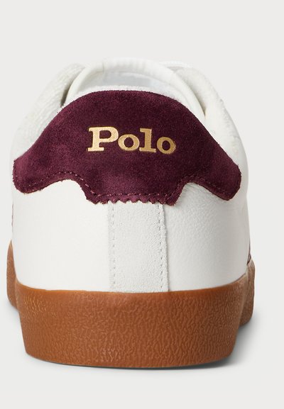 Bijele tenisice s bordo nubuk petom. Imaju teksturiranu smeđu gumenu podlogu i zlatni "Polo" logo na peti.