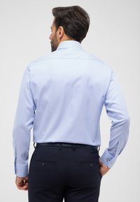 Lichtblauw overhemd met lange mouwen, een micro-patroon, button-down kraag en contrasterende knoopaccenten. Gedragen met donkere broek.