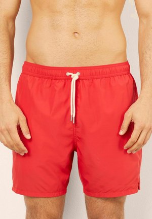 Bañador rojo hecho de un tejido ligero y resistente al agua. Cuenta con una cinturilla elástica con cordón y bolsillos laterales.