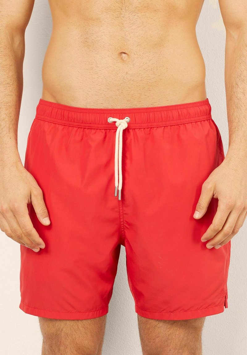 Bañador rojo hecho de un tejido ligero y resistente al agua. Cuenta con una cinturilla elástica con cordón y bolsillos laterales.