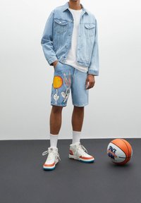 Conjunto de chaqueta de mezclilla y pantalones cortos en azul claro, con el personaje de dibujos animados Bugs Bunny. Zapatillas blancas con acentos en naranja y turquesa. Pelota de baloncesto presente.