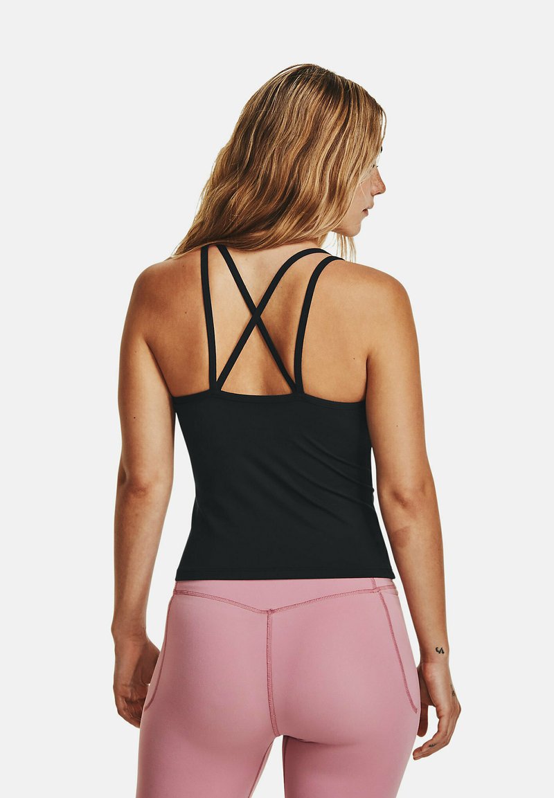 Frau mit langen blonden Haaren, die ein schwarzes Sporttop mit Trägern und rosa High-Waist-Leggings trägt, von hinten auf weißem Hintergrund gezeigt.
