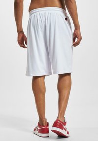 Hvite mesh basketballshorts med elastisk liv, med sidelommer og en liten svart merkevarelogo, kombinert med røde treningssko.