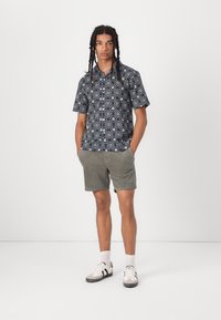 Chemise à manches courtes avec un motif floral bleu foncé, associée à un short vert clair, et des baskets noir et blanc avec des accents gris subtils.