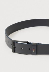 Tumši zils ādas josta ar matētu apdari, kurai ir melna metāla sprādze un neliels logotipa uzraksts uz aizdare. Gluda tekstūra, regulējamas caurumi.