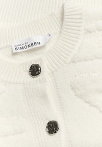 Biely pletený cardigan s rebrovaným golierom, textúrovanou tkaninou a kovovým gombíkom. Na štítku je uvedené meno značky "KAREN BY SIMONSEN", veľkosť M.