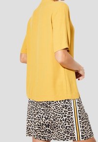 Gul kortärmad topp i kombination med en kjol i leopardmönster som har svart och vita ränder. Slät textur med en avslappnad passform.