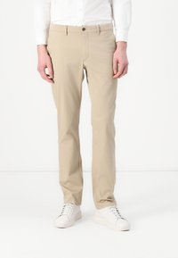 Beige Baumwoll-Chinos mit geradem Schnitt, ausgestattet mit einem Knopfverschluss und Gürtelschlaufen. Tragen Sie sie mit weißenSneakern für einen Kontrast.