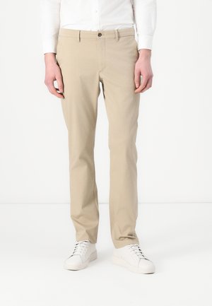 Beige puuvillased chinos sirge lõikega, nööbiga sulgemine ja vööaugud. Kanda valgete tossudega kontrasti loomiseks.