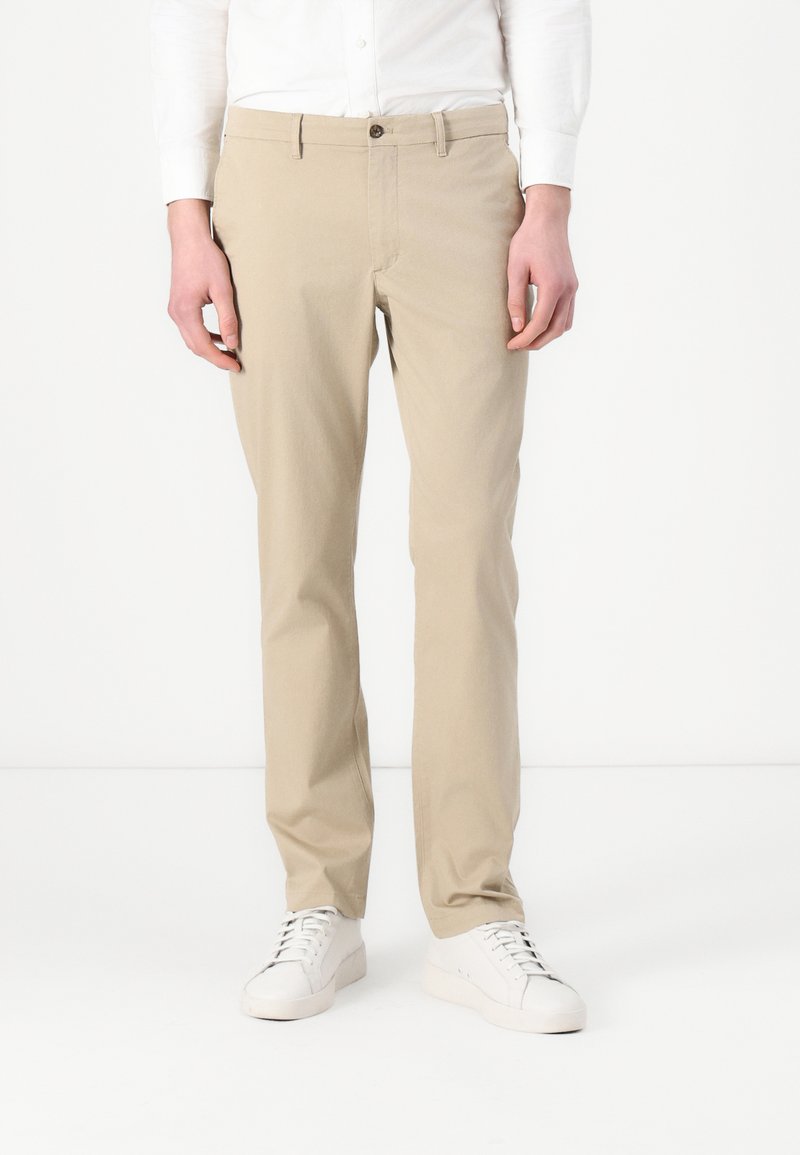 Beige Baumwoll-Chinos mit geradem Schnitt, ausgestattet mit einem Knopfverschluss und Gürtelschlaufen. Tragen Sie sie mit weißenSneakern für einen Kontrast.