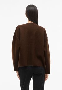 Rudas didelis megztinis su minimalistiniu dizainu, plačiomis rankovėmis, tiesiu užbaigimu ir glotnia, minkšta tekstūra.