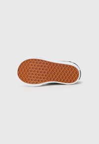 Schuh, der auf der Seite liegt und die braune Waffelmuster-Sohle mit weißem Gummi-Rand auf einem schlichten weißen Hintergrund zeigt.