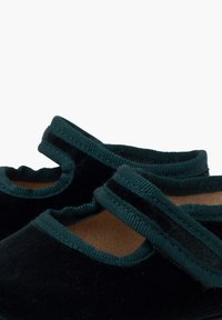 Zapatos de terciopelo negro con una correa elástica de color teal; punta redonda y laterales recortados. Textura suave con suela plana, acentuada por colores contrastantes.