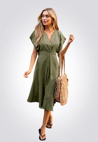 Vestido verde olivo, hasta la rodilla, con escote en V, mangas cortas y botones frontales. Combinado con un bolso de textura tejida y chanclas.