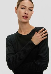 Schwarzer gerippter Strickpullover mit langen Ärmeln und Rundhalsausschnitt, mit einer figurschmeichelnden Passform und strukturiertem Stoff. Neutraler Hintergrund.