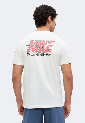 Homme portant une chemise blanche à manches courtes avec un logo "Nike Running" rose et noir dans le dos, associée à un short bleu, de dos.