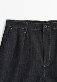 Pantalons en denim foncé avec une coupe ajustée, dotés d'une fermeture à bouton, de couture subtile et de poches latérales.
