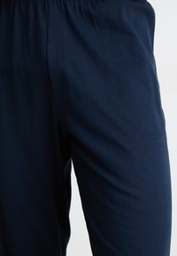 Pantalons en coton extensible bleu marine avec une taille élastique. Texture lisse et coupe ajustée, adaptés pour un port décontracté ou relax.