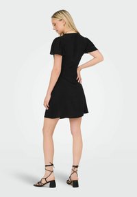 Vestido corto negro con mangas abullonadas y falda acampanada, hecho de una tela ligera. Textura transparente en el dobladillo, combinado con sandalias negras de tiras.