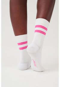 Weiße Sportsocken mit rosa Streifen, ausgestattet mit strukturierten Sohlen und gerippten Bündchen. Sie bieten eine figurbetonte Passform um die Knöchel.
