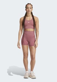 Lys pink atletisk sæt med en cropped tanktop med logo og højtaljede shorts. Modellen har beige sneakers på. Glat tekstur.