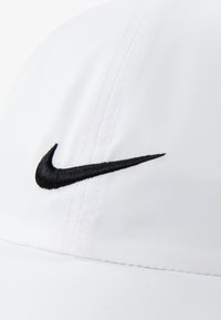 Gorra deportiva blanca de tela con el logo negro de Nike en forma de swoosh bordado en el frente, con líneas limpias y un diseño estructurado.
