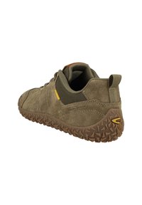 Baskets en daim vert olive avec une semelle en caoutchouc texturé, des panneaux en maille sur les côtés et un renfort au niveau du talon. Accent jaune près des lacets.