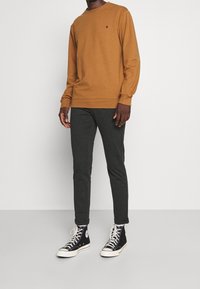 Sweat-shirt marron à manches longues avec des poignets côtelés, associé à un pantalon gris foncé fuselé et des baskets montantes noires avec des semelles et œillets blancs.
