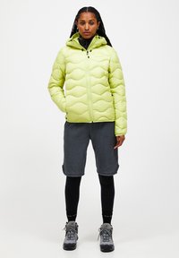 Lys grøn quiltet pufferjakke med hætte, frontlynlås og elastiske manchetter. Kombineret med grå fleece shorts og sorte leggings.