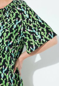 Schwarzes Kurzarmkleid mit grünem Kaktusmuster und rosa Blumen. Weicher Stoff mit lässiger Passform und gerafftem Ausschnitt.
