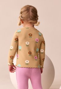 Langærmet beige striktrøje med farverige blomsterprint, ribbet tekstur og bølget kant, kombineret med pink ribbede leggings.