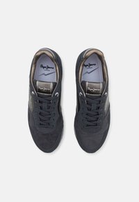 Zapatillas de ante azul marino con paneles texturizados, punta redonda, detalles grises y suela blanca contrastante. Presenta cierre de cordones y logotipo en la lengüeta.